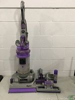 Upright Dyson Animal vacuum with wand and hose attached, attachments laid out in front.