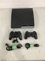 Top view of the black Sony PlayStation 3 console, two black DualShock 3 controllers, and cables.