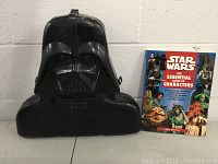 Closed Darth Vader-shaped action figure storage box next to Star Wars Essential Guide to Characters book.