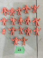 Full view of 18 vintage-style pink rubber muscle wrestler figurines arranged on a flat surface, showing their size and variety.