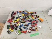 Full overview photo showing approximately 60 toy cars scattered on a table, including a mix of colors and styles.