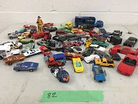 Full view of assorted toy cars, trucks, motorcycles, and a fireman figure arranged on a surface against a white wall.