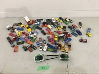 Overview of the lot showing approximately 60 assorted toy cars spread out on a white surface with two Hulk walkie talkies in the foreground.