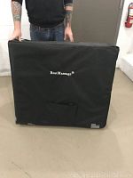 Closed portable BestMassage massage table inside its black carrying case, held by a person, with visible minor wear on bottom of case.