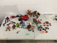 Wide view of lot showing various He-Man action figures and accessories including figures, creatures, and a red vehicle.