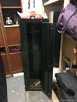 Full view of the Stack-On green metal gun safe with door open; blaze orange shirts and hats in packaging stacked on top.