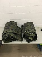 Two large rolled camouflage tarps on a folding table.