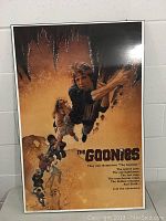 Front view of the glossy vintage 1980s The Goonies movie poster mounted on board, showing characters climbing and movie text.