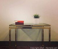 Full view of the vintage 1970s side table with brass frame and smoked glass top, styled with a potted plant and two books on top.