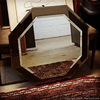 Front view of the vintage octagon mirror showing the clear central mirror with beveled edge and smoked glass surrounding frame, resting against chairs.