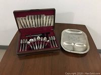 Photo showing the entire silverware set in a burgundy velvet lined case next to the metal carving tray on a wooden surface.