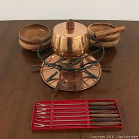 Full set displayed with copper pot on metal stand, four teak bowls behind, and six forks in red box in front