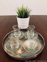 Four etched crystal glasses with matching glass saucers arranged on a round sterling silver serving tray.