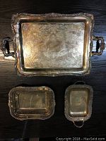 Top view of all three vintage silver serving trays showing detailed engraving and patina, arranged on wood surface
