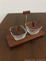 Photo showing two small crystal condiment bowls with teak lids and small teak spoons, presented on a teak tray with a central vertical handle, highlighting their Mid Century Modern design.