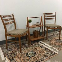 Two vintage Danish teak dining chairs displayed with a small teak and glass table in between. Chairs have slatted backs and beige cushions.