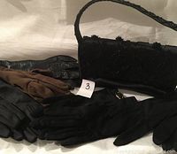 Photo showing four pairs of gloves and a black vintage purse decorated with beads and sequins, featuring a single strap and magnetic closure.