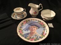 Full view of the five china pieces including commemorative plate, tea cup and saucer, creamer, and sugar bowl