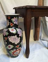Side view of the tall black floral vase beside the wood table leg showing detailed carved feet.