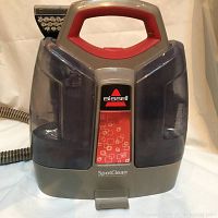 Front view of Bissell SpotClean portable spot cleaner showing large ergonomic red handle, transparent water tanks on both sides, and model label spot clean in center.