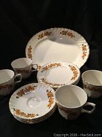 Front view of all items including cups, saucers, side plates, and serving plate arranged in front of black background.