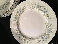 Close-up of one plate showing blue floral pattern with green foliage on white fine bone china with scalloped edge.
