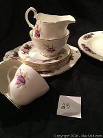 Tea cups, saucers, dessert plates stacked with cream pitcher and sugar bowl on top showing floral and gold details