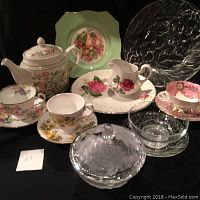 Photo showing mix of china tea cups, saucers, teapot, glass dishes, candy dish and dessert plates arranged on black background