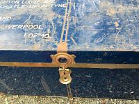 Close-up of the metal latch and partial white stamped text on the blue trunk lid, showing wear and some rust on the metal components.