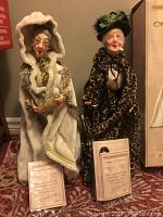 Two Jacqueline Kent Carolers dolls Miss O'Hare and Rambling Rose standing with their certificates of authenticity in front of them.