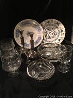 Full lot showing silver candlesticks, brandy glasses, crystal serving dishes, and two blue and white china plates with floral and pastoral designs.