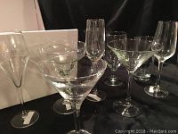 Photo showing multiple clear bar glasses including margarita, champagne, brandy and liqueur glasses arranged on black surface