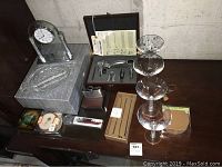 View of glass clock with etched design, four martini glasses stacked, bar accessories, metal flask, cork coasters, and serving dish on a wooden surface.