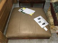 Top-down view of the olive green ostrich leather ottoman, showing texture and size with paperwork on top.
