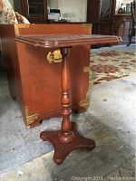 Photo showing full wooden stand with decorative top and pedestal base placed in front of the wood chest.