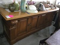 Full side view of the granite top wooden buffet cabinet with four paneled doors and decorative carvings on the corner.