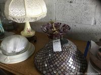 Four lamps and light fixtures including Tiffany style glass shade and purple glass ceiling fixture on a wooden surface.