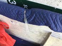 Rectangular marble slab wrapped with protective blue quilted moving blanket and secured with clear plastic wrap, showing veining pattern on surface and edges