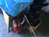 Red Miele canister vacuum cleaner with hose and wand next to cardboard boxes
