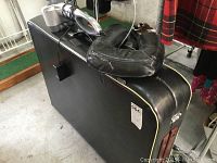 Closed black portable massage table with yellow piping and handle, placed on floor.