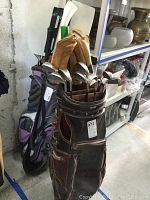 Brown golf bag and black/purple golf bag both holding golf clubs in storage area