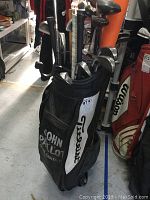 Photo of a black John Pallo Titleist golf bag filled with golf clubs including irons and drivers