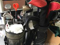 Two golf bags filled with various golf clubs including irons and woods, one bag has multiple zippered compartments and a logo