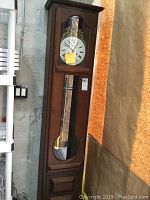 Full view of the tall dark wooden grandfather clock with glass panel and carved wood bottom.