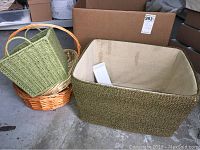 Large rectangular green woven basket with beige fabric lining, alongside smaller woven baskets in natural and green colors.