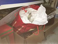 Red storage bag with Christmas decorations inside, including some white tissue paper used for wrapping or padding items.