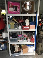 Full view of 4-tier shelf with assorted small bags, boxed bonnet dryer, round magnifying mirror, and haircurlers.
