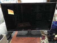 Samsung flat screen TV with stand on a glass surface, front view.
