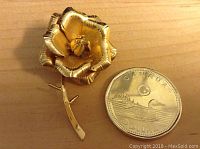 Front view of the gold filled rose brooch next to a Canadian dollar coin for size comparison. The brooch features detailed petals and stem shape.