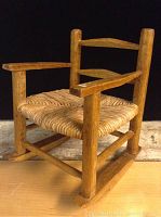 Handmade miniature wooden rocking chair showing front and side view, highlighting woven seat and wood construction.